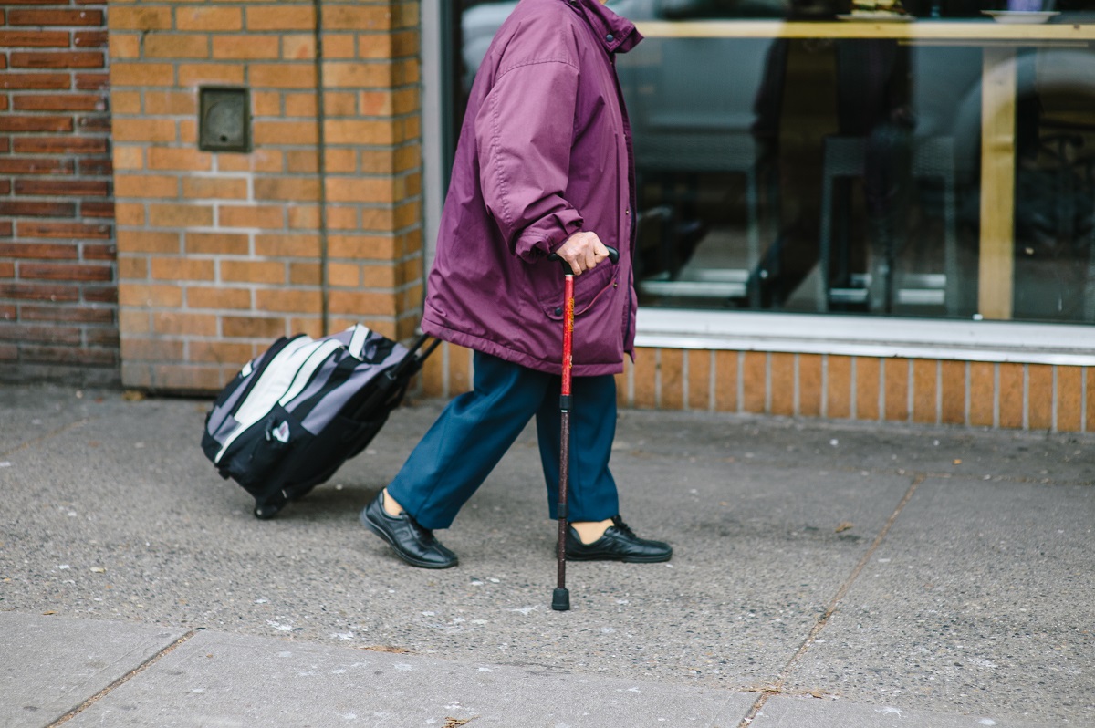 Senior walking with cane and bag