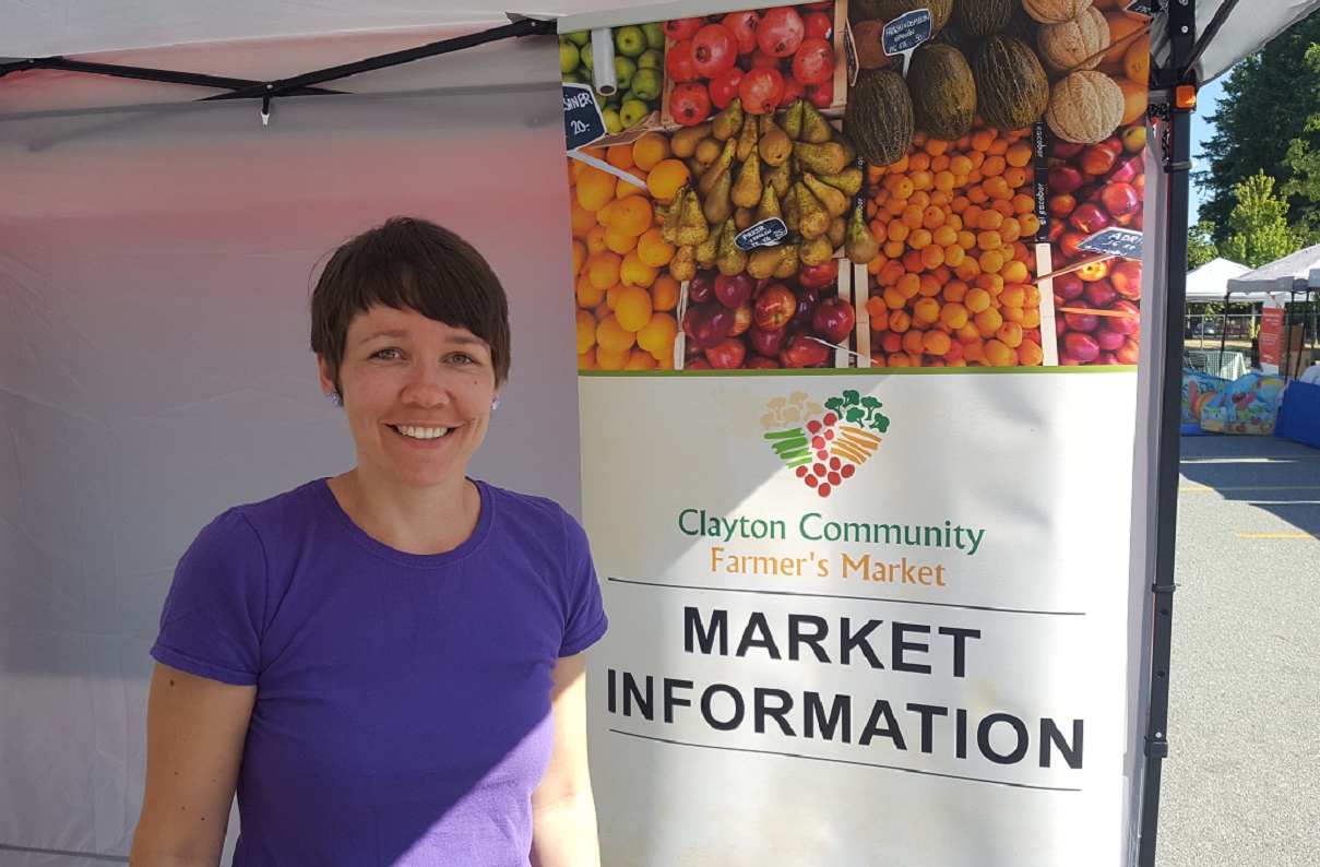 Sabrina Mehlhorn is the founder and organizer of the Clayton Community Farmer's Market. She stand in front of a market banner.