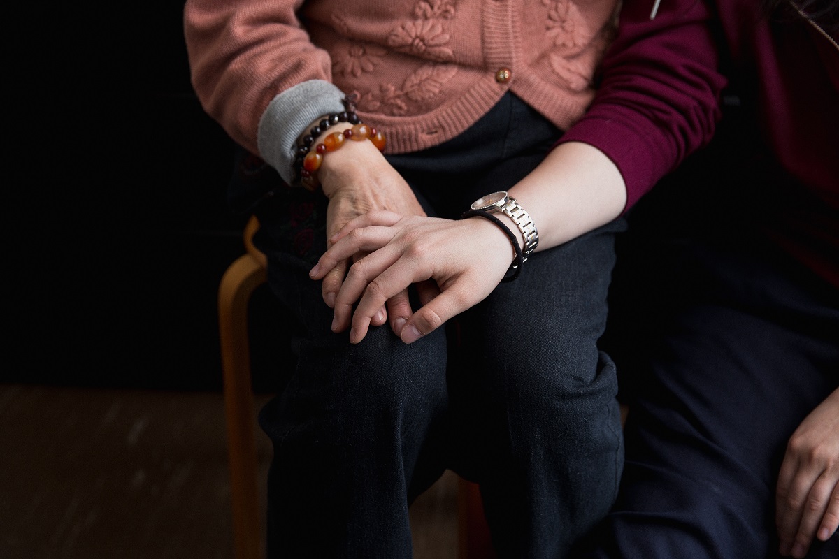 Two hands hold each other. One is from an older woman and the other is from a young woman.