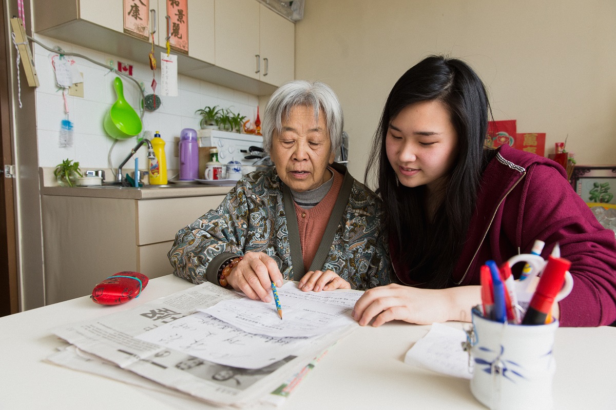 An older woman and a young woman sit at a table together, looking at a piece of paper.