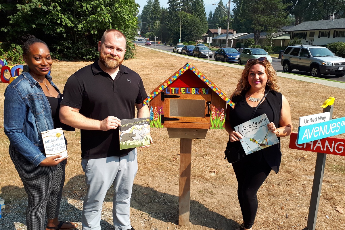 Three people stand in front of a little library in Port Coquitlam.