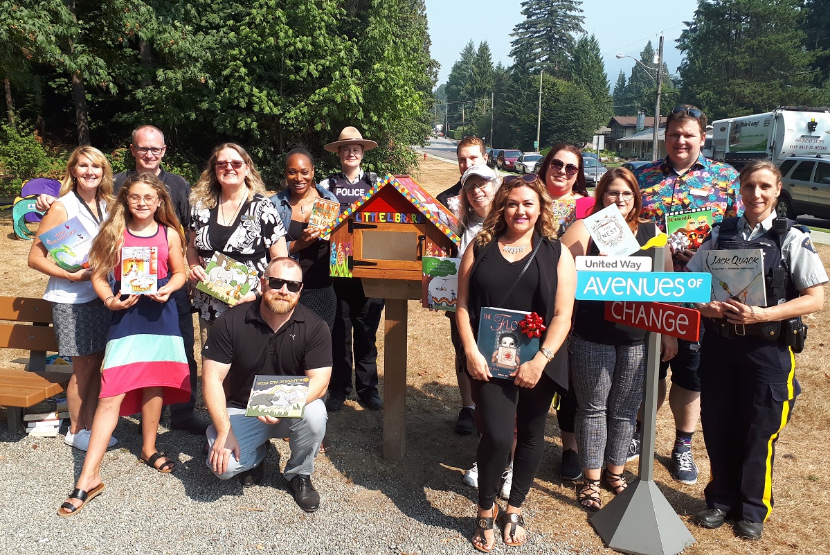 A group of people stand in front of a little library.