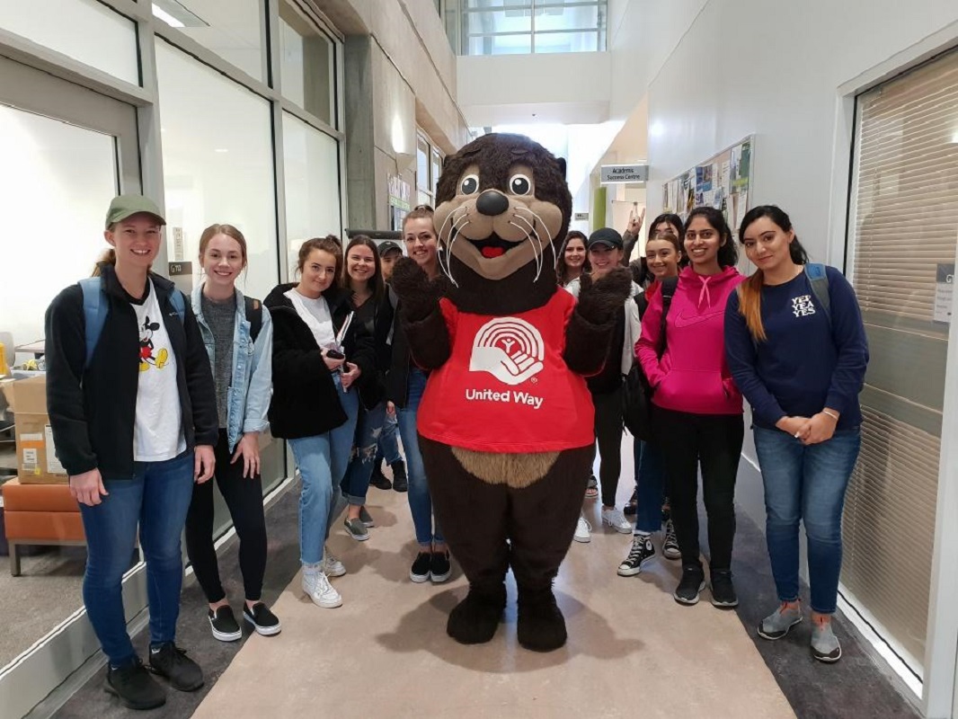 A group of people stand and smile with a sea otter mascot.