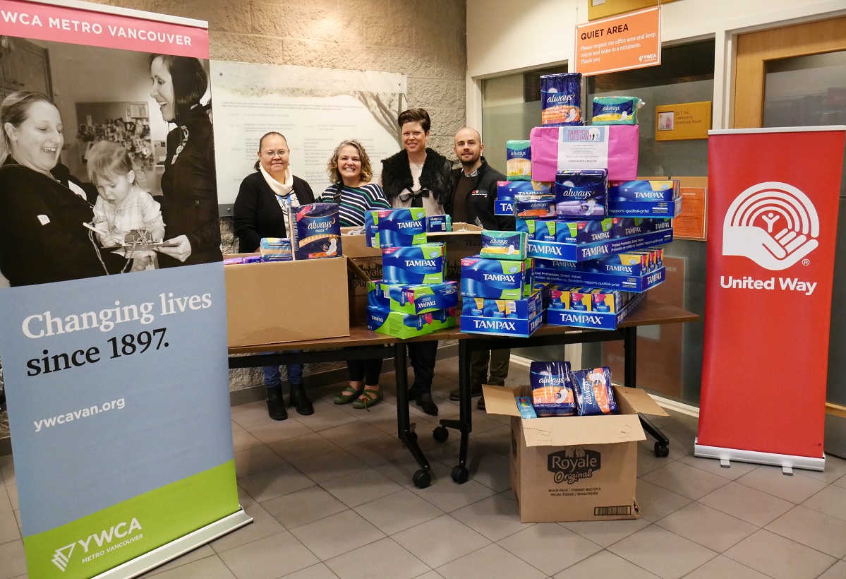 Four individuals stand behind a table that is stocked with menstruation products.