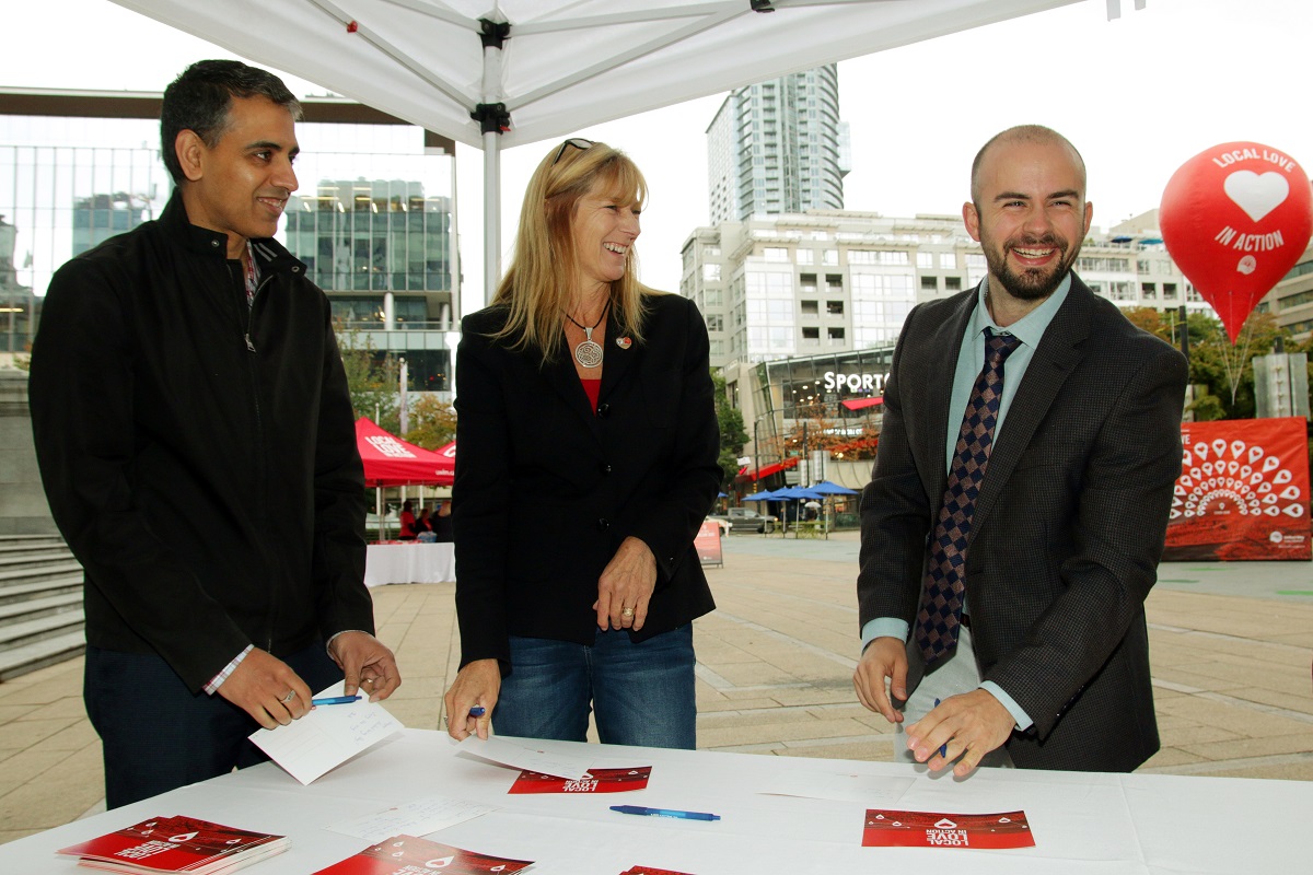 Three people write cards and smile at the camera.