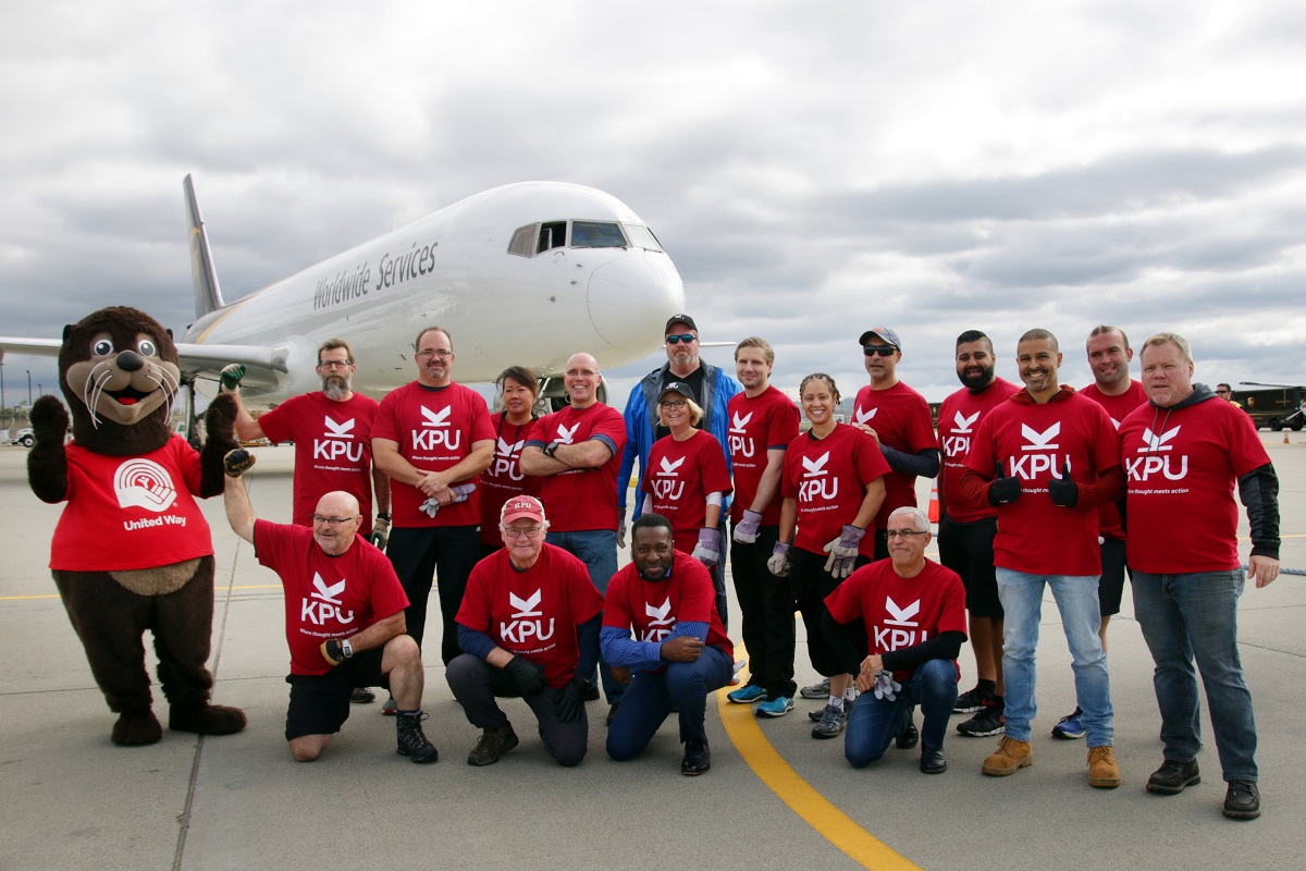 A team of men and women wearing red shirts smile in front of a plane.