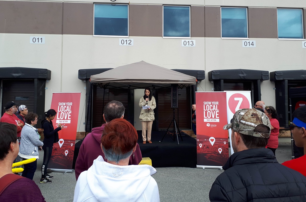 A young woman stands on a stage in front of a crowd and speaks into a microphone.