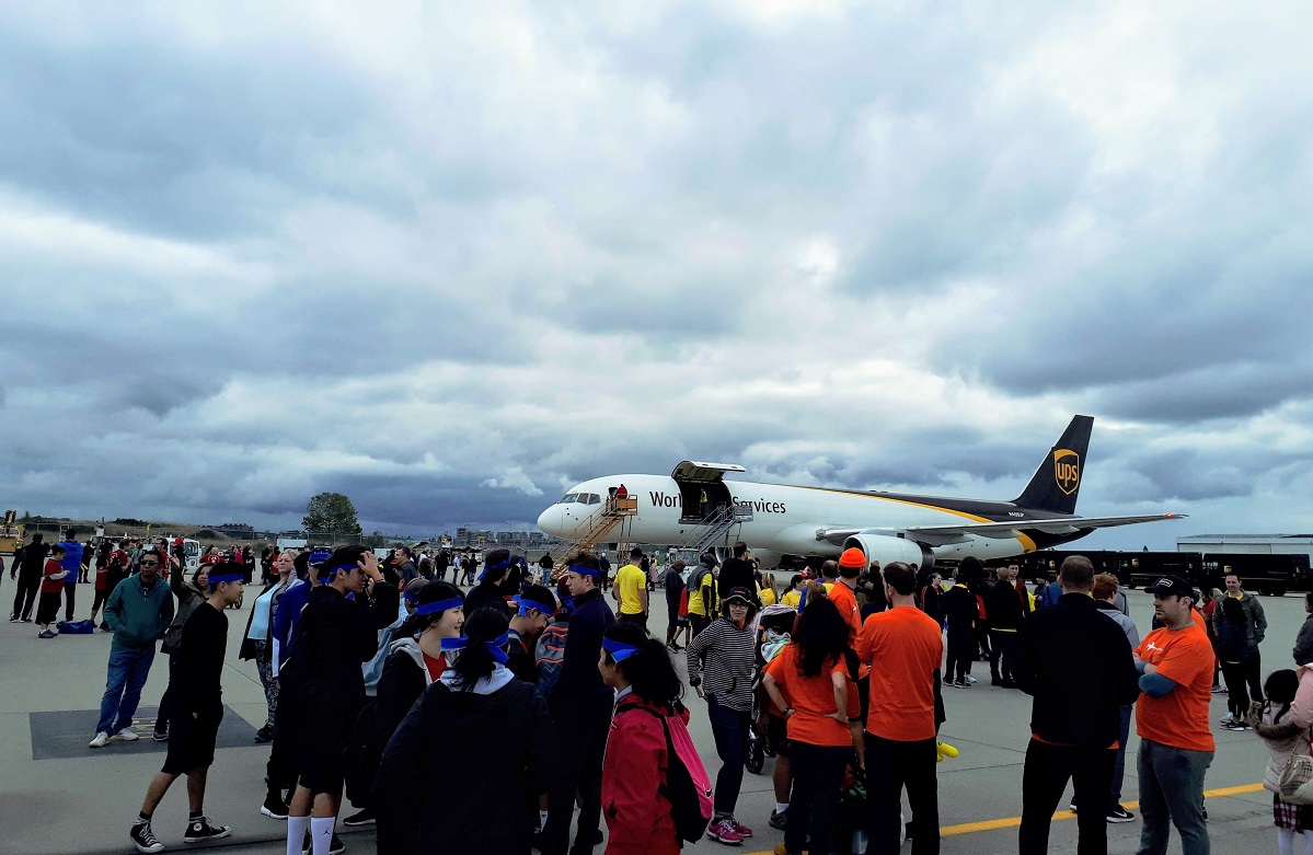 A large group stands on an airport tarmac in front of a UPS cargo plane.