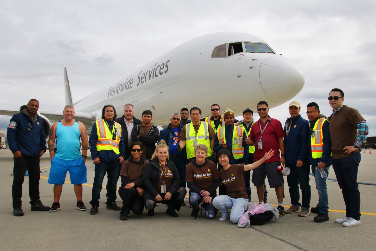 A group of UPS workers pose for a photo in front of a cargo plane.