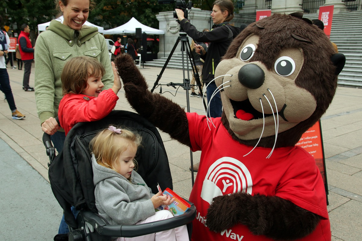 A smiling family laughs with a large otter mascot.