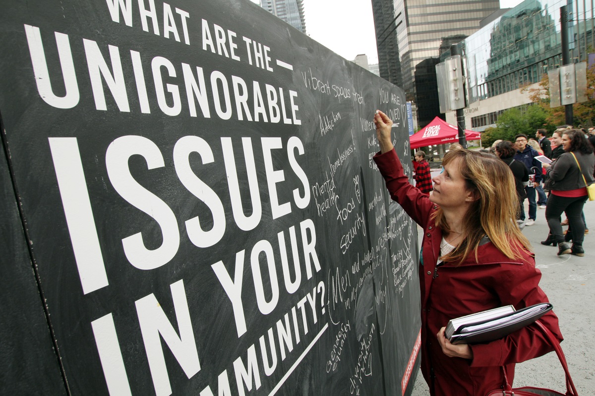 A woman stands in front of a large chalk board and writes in white chalk.