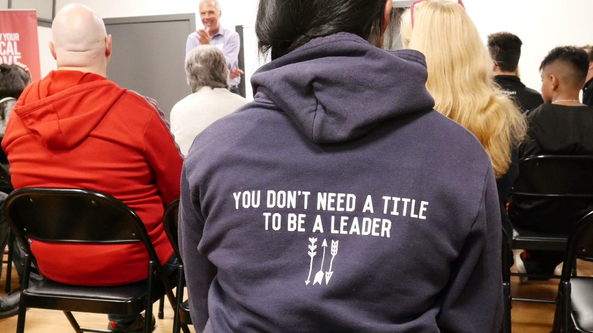 A teenager sits wearing a purple hoodie with "You don't need a title to be a leader" written on it.