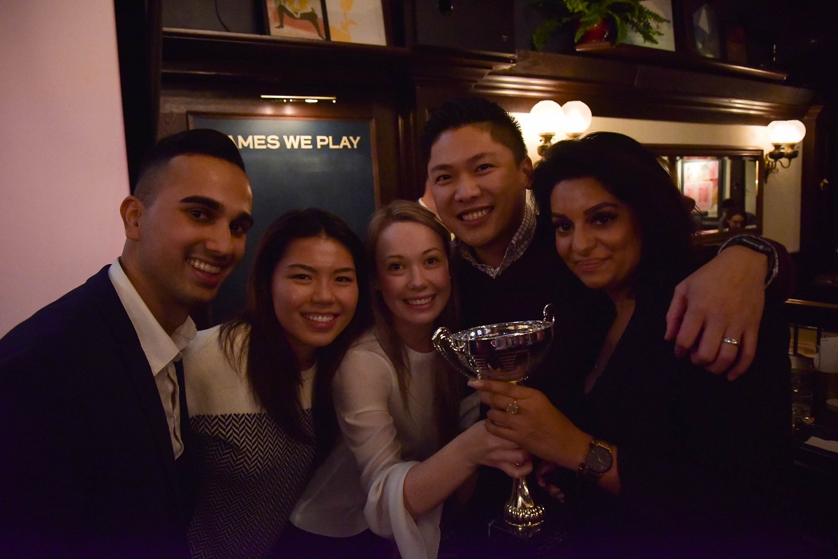 A group of smiling people huddle around a large trophy.