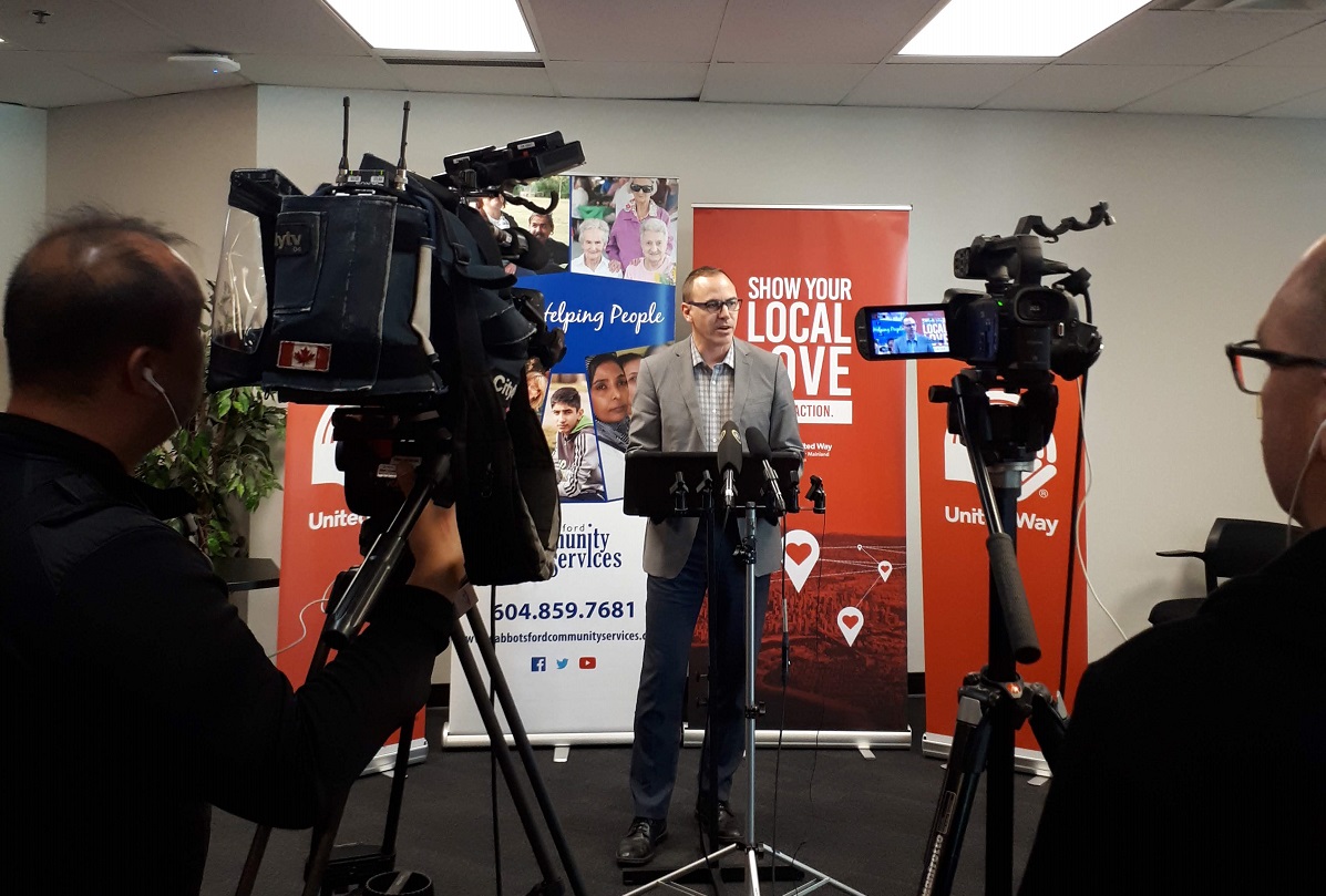 A man speaks from a podium to a room full of cameras.