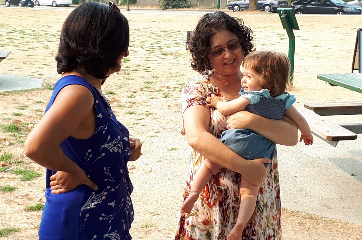 Two omen in a park. One of them holds a baby.