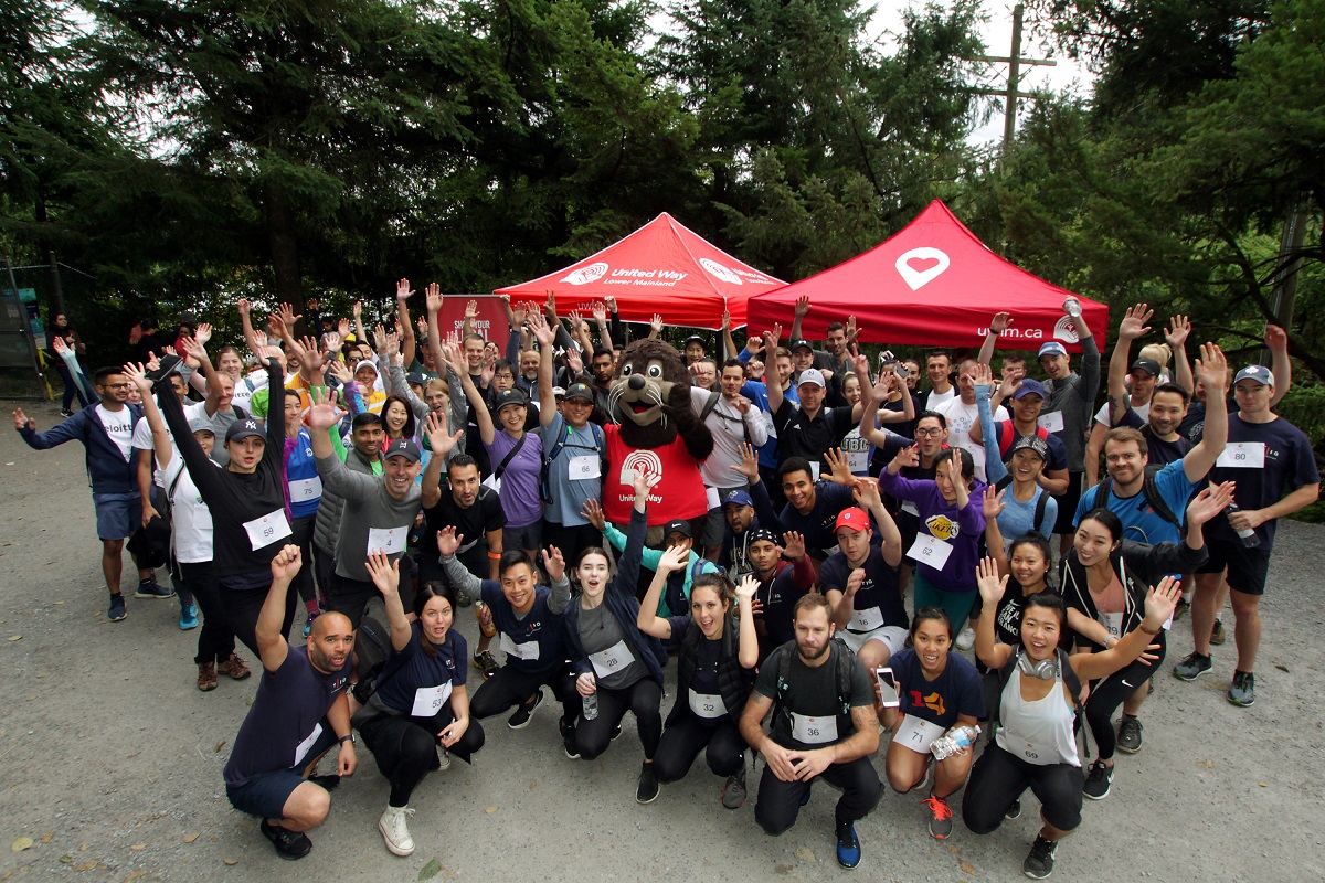 A group of people outfitting in athletic gear post at the base of Grouse mountain.