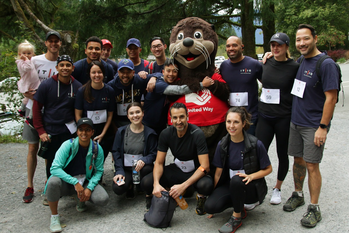 A group of people wearing identical shirts poses for the camera with a sea otter mascot.