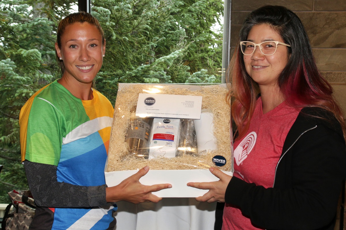 Two women smile at the camera holding a coffee prize pack.