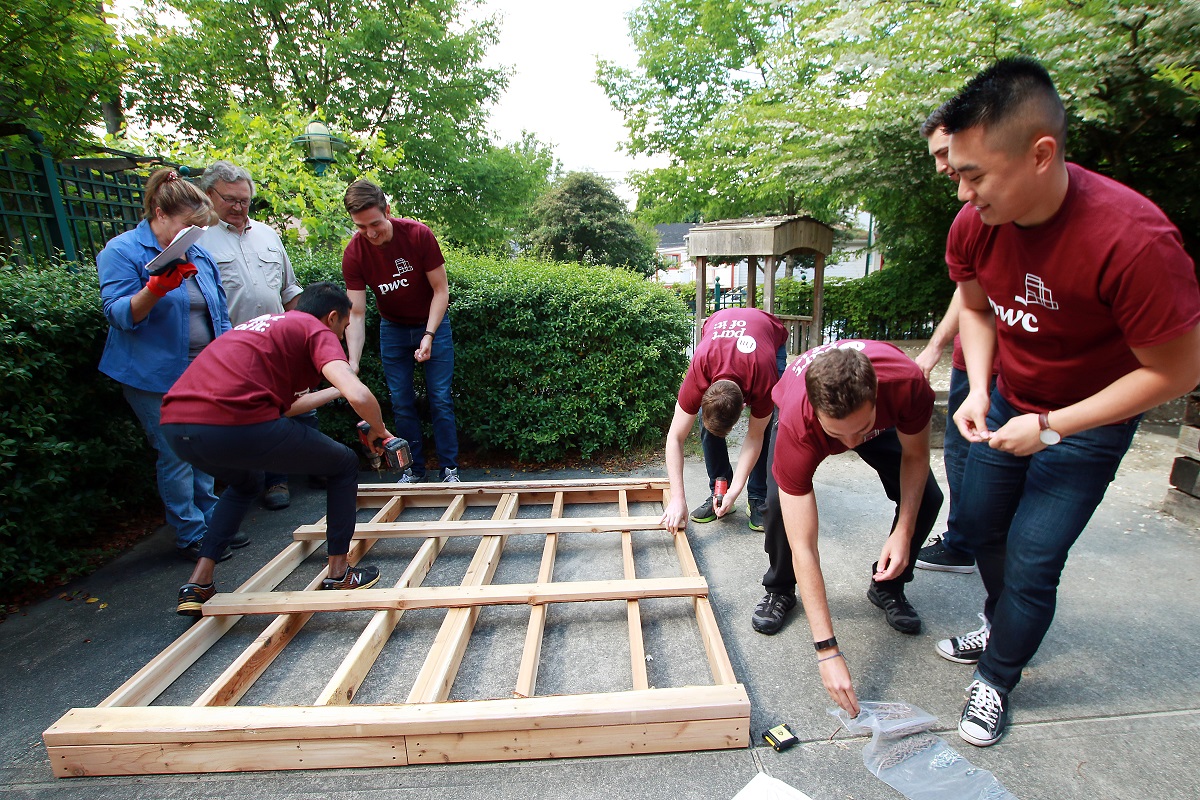 Men and women work together to nail together wooden planks.