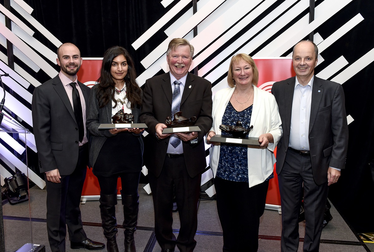 Five individuals smile and pose on stage at an event.