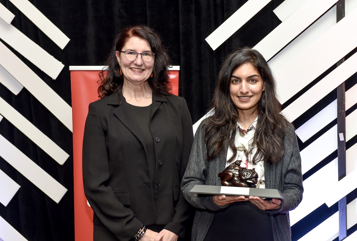 Two women smile at the camera. One holds an award.