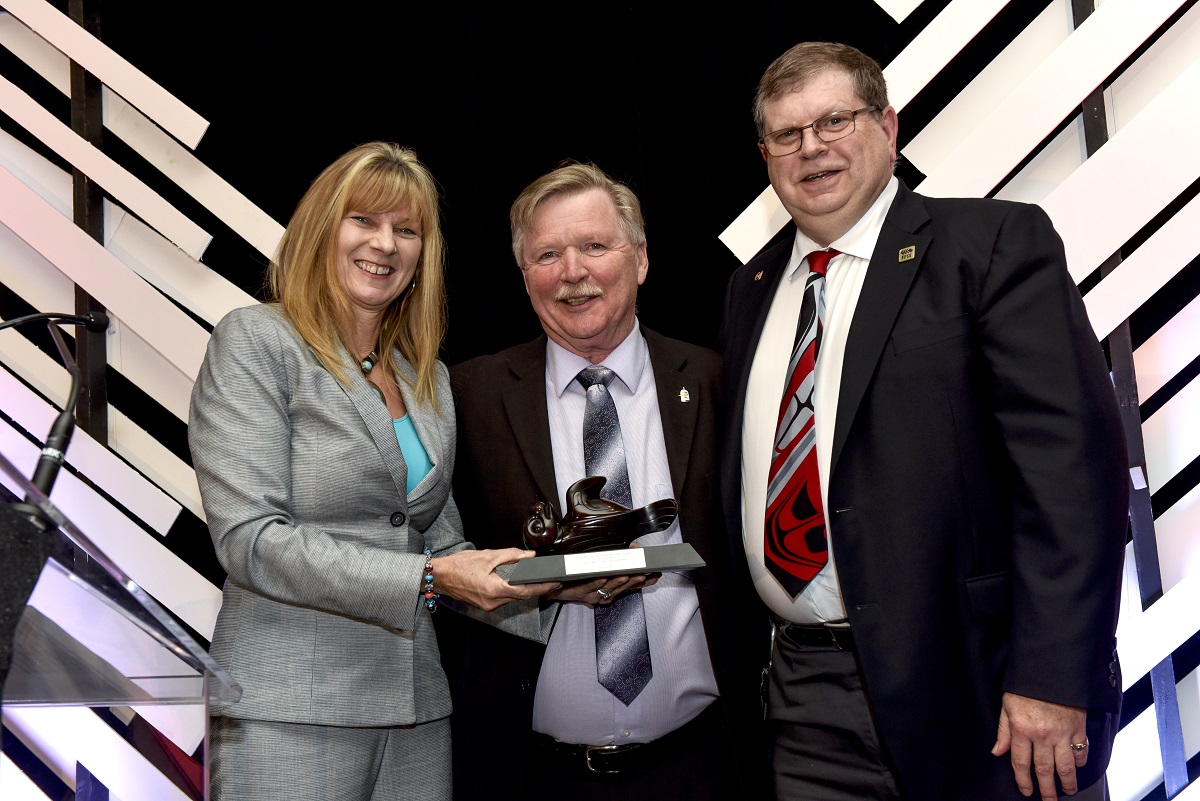 A woman and two men smile at the camera, celebrating an award.