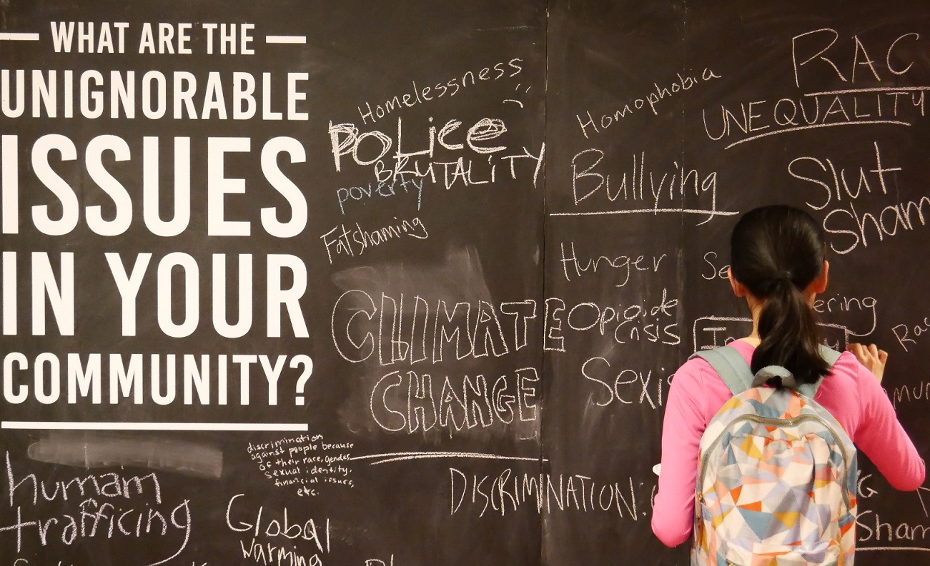 A young woman writes at a large chalkboard.