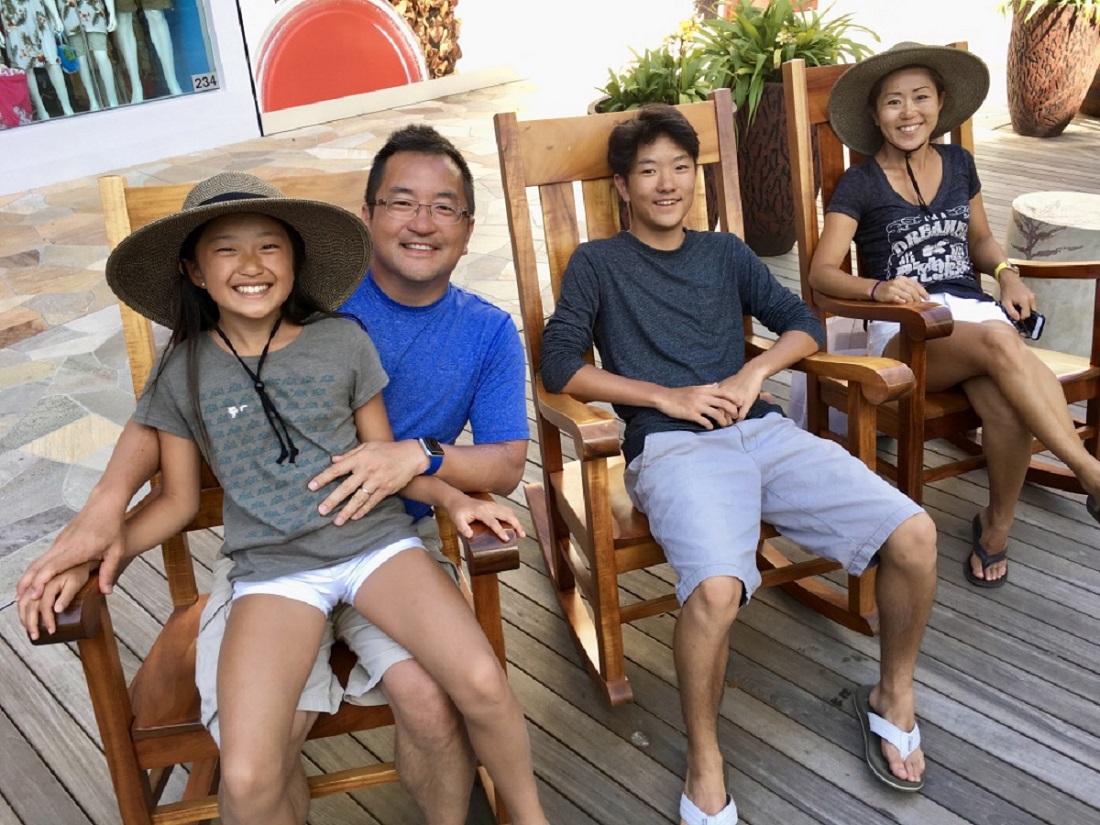 A smiling family sits on deck chairs.