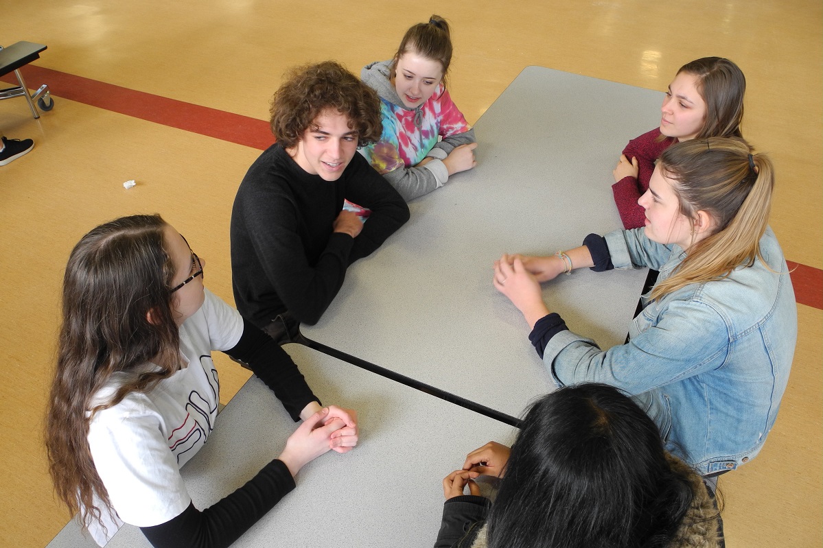 A group of teenagers sit at a table chatting.